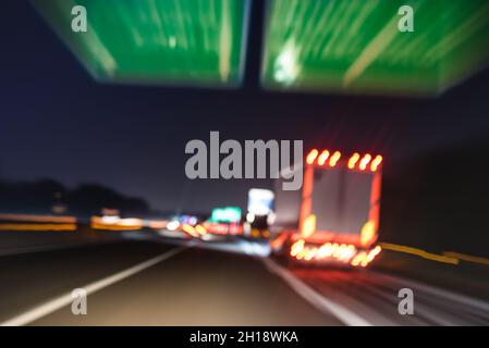Defocused blurred motion of semi truck speeding on highway under street signs - Night traffic and transport logistic concept with semitruck container Stock Photo