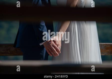 young Caucasian bride wearing a silky white dress and groom in a dark blue suit holding hands, a beautiful couple having a moment of intimacy Stock Photo