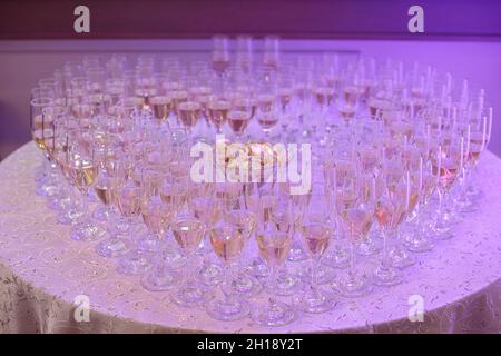 Full glasses of bubbly or champagne forming a heart shape, positioned on a round table under a neon purple light, a typical wedding reception or party Stock Photo
