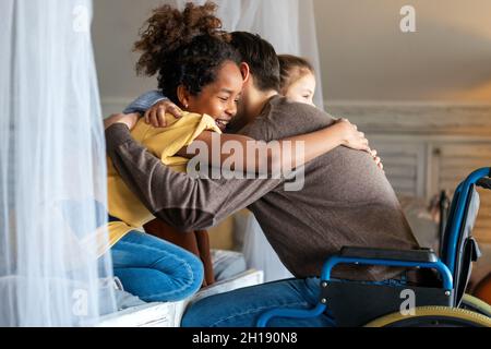 Portrait of happy loving father with disability in wheelchair hugging with multiethnic children Stock Photo