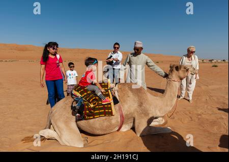 Tourists taking a ride on a camel's back.   Wahiba Sands, Arabian Peninsula, Oman. Stock Photo