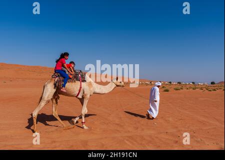 Tourists taking a ride on a camel's back. Wahiba Sands, Arabian Peninsula, Oman. Stock Photo