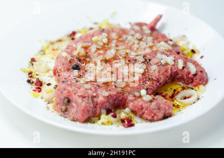 Minced meat with fresh spring onions and spices in the shape of a pig on the white plate, a creatively prepared burger in an interesting shape, funny Stock Photo