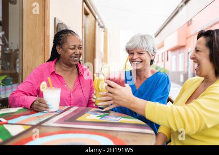 Multiracial senior women having fun cheering with healthy drinks at brunch restaurant - Focus on african woman Stock Photo