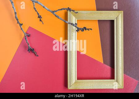 Empty wooden frame made of beech and tree branch without leaves on multi-colored abstract paper background. Red, orange, brown. Place for photo. Stock Photo