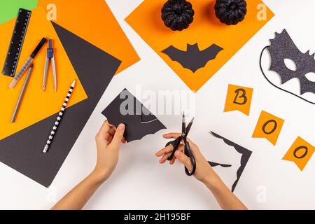 Preparing for Halloween. Teenage kid hands cutting black paper bat