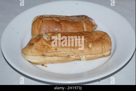 A close-up shot of a couple of hot dogs stuffed with cheese on a white plate Stock Photo