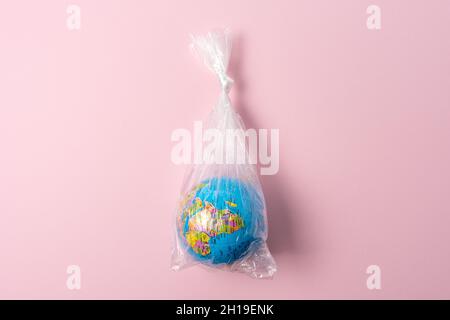 Earth globe in plastic bag on pink background. Minimal ecology concept. Stock Photo