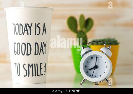 White alarm clock with a paper cup of coffee on wooden desk. Minimal time concept. Stock Photo