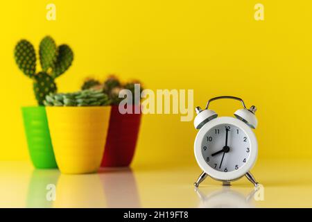 White alarm clock with cactus in pot on wooden desk. Minimal time concept. Stock Photo