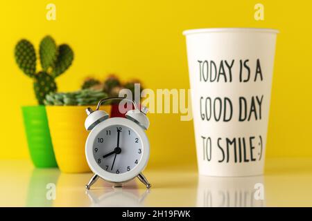 White alarm clock with a paper cup of coffee on wooden desk. Minimal time concept. Stock Photo