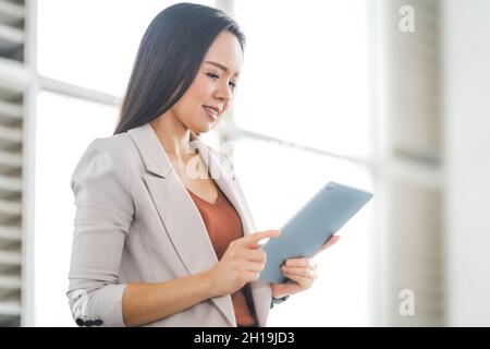 A cheerful Thai young businesswoman working on her tablet in the office Stock Photo