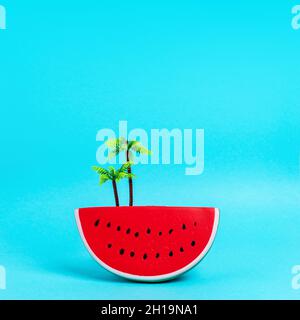 Watermelon fruit with palm tree plastic toy on pastel blue background. Creative minimal summer concept. Stock Photo