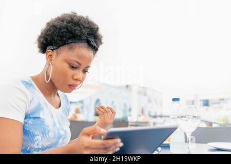 A serious adult woman sitting on a outside restaurant using and looking her digital tablet Stock Photo