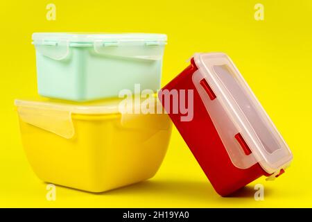 Multicolored plastic lunch boxes on yellow background, side view. Food containers of different shapes and sizes Stock Photo