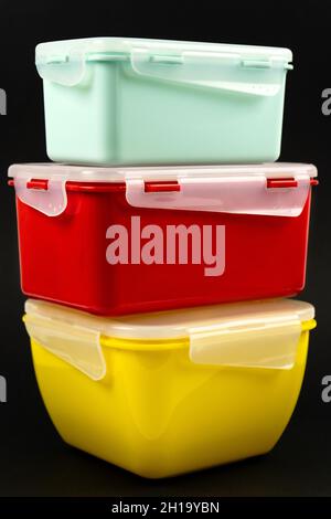 Yellow, mint and red plastic lunch boxes on a black background. Vertical photo Stock Photo