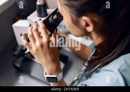 Scientist looks into microscope researching material sample at table in laboratory Stock Photo