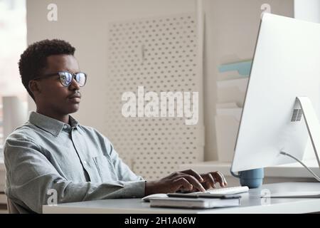 Minimal side view portrait of young African-American man using computer and writing code in software development office, copy space Stock Photo