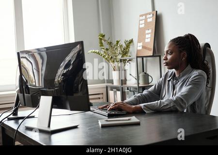 Side view portrait of successful African-American woman using computer while sitting at desk in office, female CEO concept, copy space Stock Photo