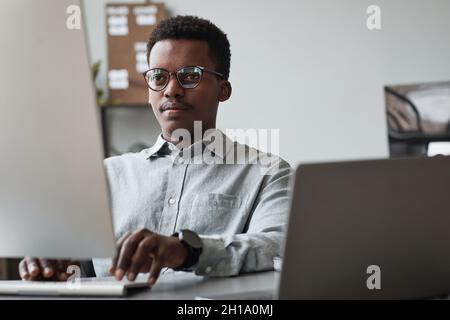 Front view portrait of young African-American man using computer and writing code in software development office, copy space Stock Photo