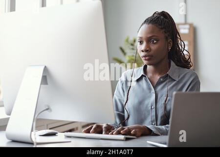 Portrait of young African-American woman using computer and writing code while working in software development office, copy space Stock Photo