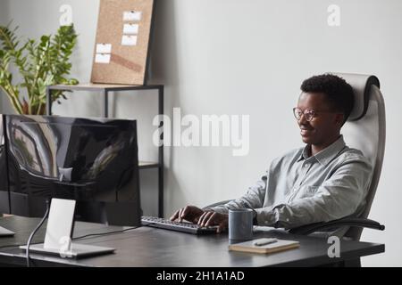 Portrait of smiling African-American man using computer while sitting at desk in office, software developer concept, copy space Stock Photo