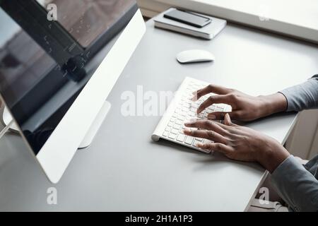 Minimal close up of unrecognizable African-American woman using computer while working at desk background, focus on hands typing at keyboard, copy spa Stock Photo
