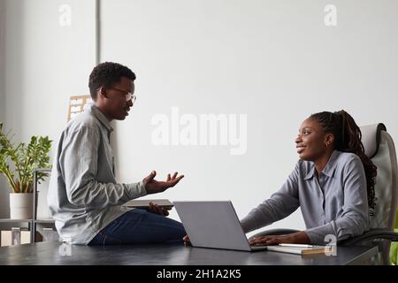 Minimal side view portrait of two African-American young people chatting in office while discussing work project by computers, copy space Stock Photo