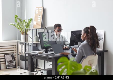 Portrait of two African-American young people using computers and writing code while working at desk in minimal office interior, copy space Stock Photo