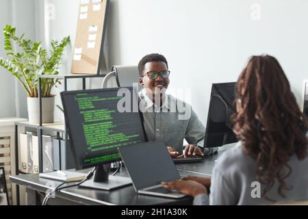 Portrait of smiling African-American man talking to colleague across table while working together in software development office, copy space Stock Photo