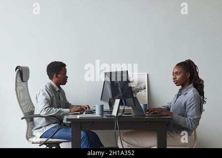 Minimal side view portrait of two African-American young people using computers and writing code while working in software development office, copy sp Stock Photo