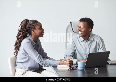 Minimal portrait of two young African-American colleagues collaborating on project and smiling while using laptop together in office, copy space Stock Photo