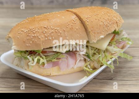 Handmade from fresh ingredients club sandwich with turkey, ham, swiss cheese, lettuce, bacon, and tomatoes, in a oven baked bun. Stock Photo