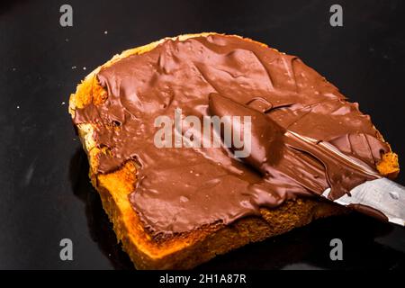 Closeup shot of spreading chocolate cream on a toasted bread slice; black background Stock Photo