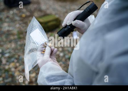 Close up back view on hands of unknown man forensic police collecting evidence in the plastic bag at the crime scene Stock Photo