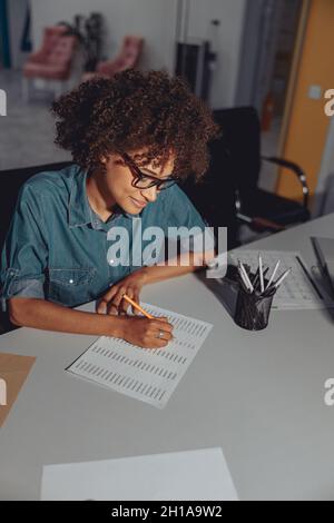 Young multiethnic lady making notes on document Stock Photo