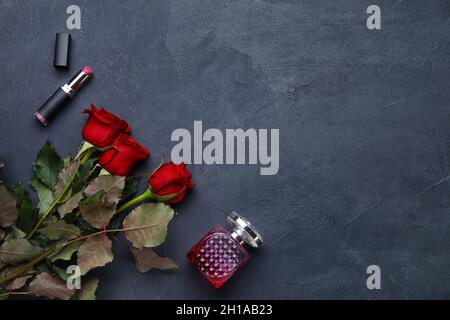 Beautiful red roses, perfume and lipstick on dark background Stock Photo