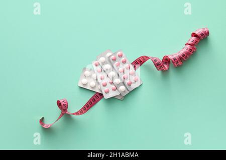 Different pills and measuring tape on color background. Weight loss concept Stock Photo