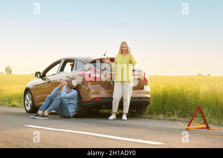 Stressed mature couple calling for help near damaged car outdoors Stock Photo