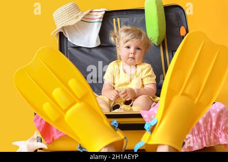 Cute baby girl in suitcase with belongings on color background Stock Photo