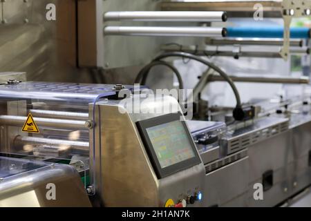 Automatic food packaging line with control panel of wrapping machine in foreground. Selective focus. Stock Photo