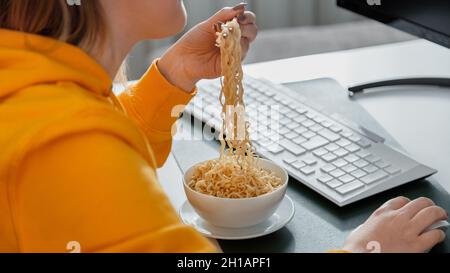 Woman gamer eats noodles with chopsticks Chinese dish in workspace interior using on the table with desktop pc computer during streaming video game Stock Photo