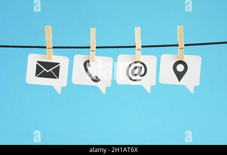 Website contact page concept banner with black contact us web icons and symbols on white paper speech bubbles hanged on blue background. Stock Photo