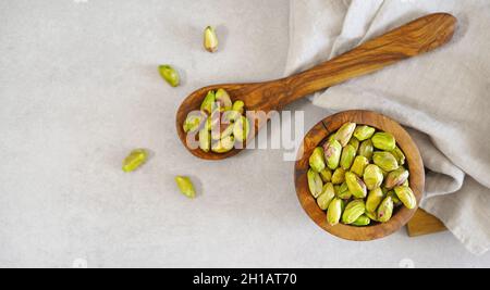 Pistachio nuts in a wooden rustic bowl and others pistachios on a wooden spoon top view overhead shot on light gray table on background. Stock Photo
