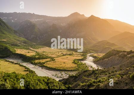 Amazing sunset over the green river valley surrounded by rocky mountains Stock Photo