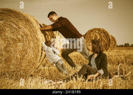 Happy young father and his two year old baby girl pushing a hay bale in harvested field Stock Photo