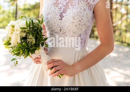 Beautiful wedding bouquet of flowers in hands of the bride. Bride holding elegant bouquet made of white roses and greenery. Stock Photo