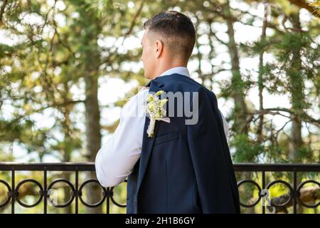 Unrecognizable young groom in elegant dark blue suit with beautiful white roses boutonniere. Groom fashion detail shot. Stock Photo