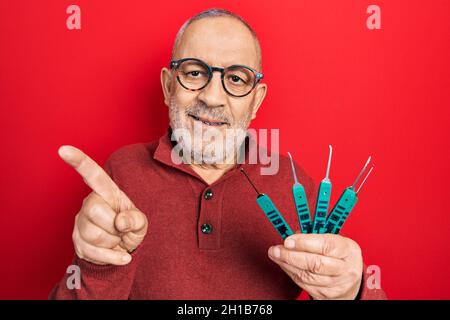 Handsome mature man holding picklock to unlock security door smiling happy pointing with hand and finger to the side Stock Photo
