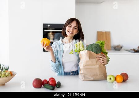 Healthy diet and lifestyle. Happy young lady unpacking paper bag with fresh organic vegetables, greens and fruits Stock Photo